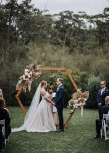 Bride Aleisha and groom Mitchell exchanging vows under a wooden hexagon arbor at their Growwild Wildflower Farm ceremony.
