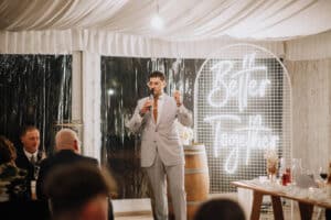 MC Alex Pisani from Unity Entertainment addressing guests at Aleisha and Mitchell's wedding reception in front of a 